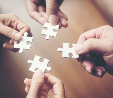 Hände verschiedener Personen fügen Puzzleteile zusammen, Sinnbild für Kooperation, Partnerschaft, Teamarbeit, Vernetzung und gemeinsames Wachstum.